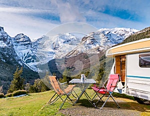 An idyllic caravan setup with chairs facing a stunning view of snow-capped mountains