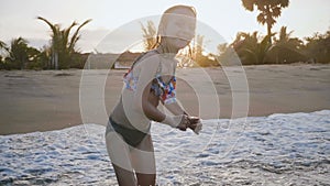 Idyllic close-up shot of happy little 5-7 year old Caucasian girl playing in ocean water waves near exotic sunset beach.