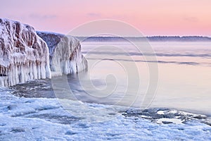 Idyllic frozen huge rock in the middle of the sea with pink sky on the horizon