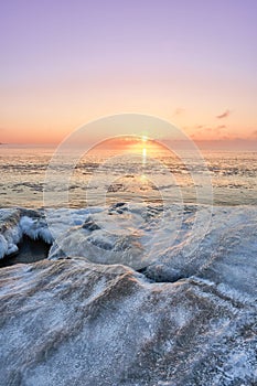 Idyllic frozen rocky shore with pink sunset sky on the horizon, perfect for wallpapers