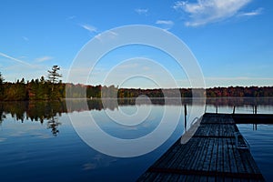 Idyllic image of an empty dock on a tranquil lake surrounded by lush trees in the fall season