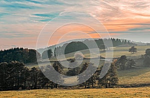 idyllic landscape like an oil painting blue sky in soft pink tones over an autumn landscape of fields and trees