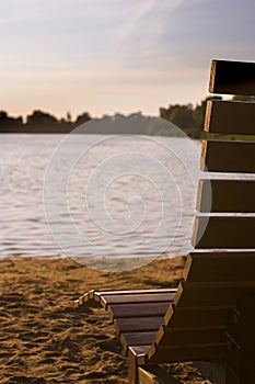Idyllic and meaningful beach scene with a view of a lake against the sun, a wooden bench in the foreground and a sandy beach in