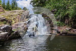 Idyllic mountain creek waterfall cascading down the cliff