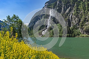 Idyllic mountain landscape in the Alps with blooming flowers, mountain lake and waterfall