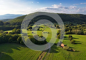 idyllic nature landscape with meadow and cottage in green hills mountain from drone