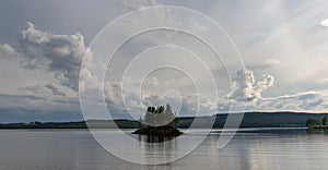 Idyllic panorama lake landscape with a small island with trees under an expressive sky