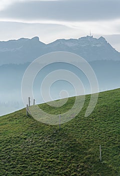 Idyllic and peaceful mountain landscape with a wooden fence on a grassy hillside and a great view of the Swiss Alps behind