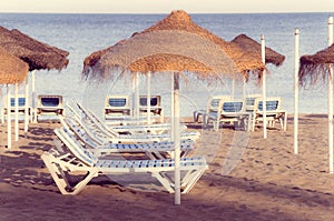 Idyllic seaside scene featuring two beach chairs and two large thatched umbrellas set up in the sand