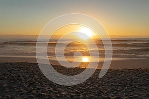 Idyllic shot of orange sun setting over sea seen from beach