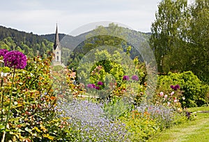 Idyllic spa garden Schliersee with view to St. Sixtus church, colorful flowerbed