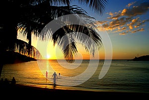Idyllic sunset at a calm bay on roatÃ¡n island with three tourists standing in the shallow water and enjoying the last sunrays of