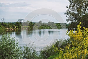 View of a calm, rural scene with a wide river reflecting the peaceful, verdant greenery of the countryside photo