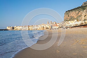 Idyllic view of Cefalu from the long sandy beach. Cathedral and Rocca di Cefalu rocky mountain on a sunny day in Cefalu, Sicily,