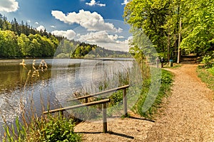 Idyllic view at a lake with reflecting white clouds at blue sky at springtime with a railing into the lake as foreground