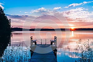 Idyllic view of the long pier with wooden bench on the lake. Sunset or sunrise over the water