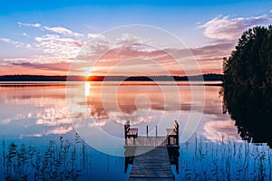 Idyllic view of the long pier with wooden bench on the lake. Sunset or sunrise over the water