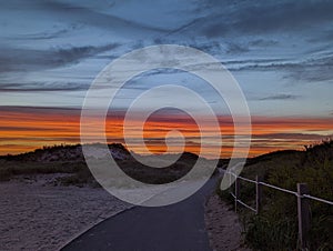 Idyllic view of a winding paved road snaking through sand dunes, illuminated by a beautiful  sunset