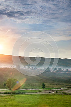 Idyllic village in foggy under sky with clouds and sunrise