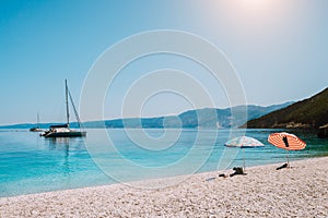 Idyllic white beach with umbrellas on lazy summer day. Sailing boat on calm crystal clear water