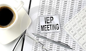 IEP MEETING text on sticky on the chart with coffee,pen and calculator