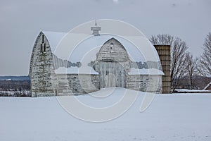 Old rugged white barn covered in snow