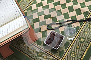Iftar time dried dates holy Quran glass of water and tasbih on praying rug or sejadah