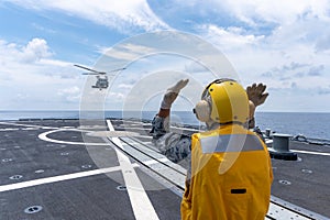 Signal man gives the hand signal to Sikorsky MH-60S Seahawk helicopter to land on the flight deck of the HTMS. Bhumibol Adulyadej