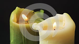 Igniting candles on black background close up. Green and white natural wax candles filmed in high framerate.