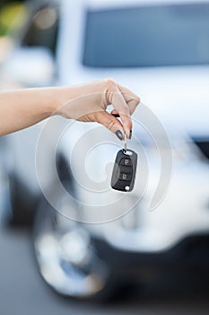 Ignition key hanging in female hand with defocused car