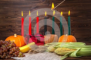Ignition of Kwanzaa traditional candles, holiday concept with gift box, pumpkins, ears of wheat, grapes, corns, banana, bowl and