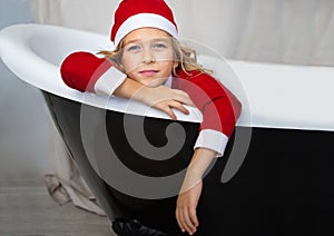 Iittle girl in Santa Ð¡hristmas hat is sitting in a bathtub