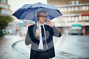 Ill be in the office soon. Shot of a mature businessman talking on a cellphone and holding an umbrella while out in the