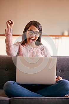 Ill be spending my weekend online. an attractive young woman using a laptop on the sofa at home and cheering.