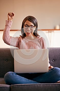 Ill be spending my weekend online. an attractive young woman using a laptop on the sofa at home and cheering.