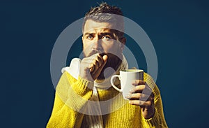 Ill bearded man with flu and fever drinking medicine tea. Handsome guy having sore throat. Sick man in sweater wrapped