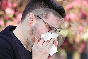 Ill boy with flu is sneezing in the park