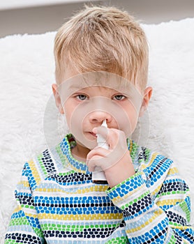 Ill boy with flu using nose spray