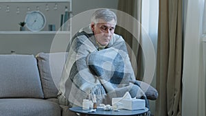 Ill caucasian elderly grandpa sit in covered with blanket on couch at home with cold remedy unhealthy senior adult man