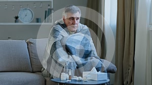 Ill caucasian elderly grandpa sit in covered with blanket on couch at home with cold remedy unhealthy senior adult man