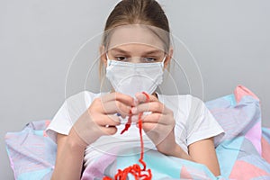 Ill girl in a medical mask knits lying in bed