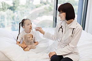 Ill girl resting on bed while doctor measuring temperature