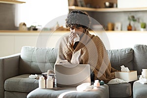 Ill indian man covered in blanket looking at laptop and sneezing nose