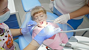 Ill kid with aching teeth lies on dental chair at inspection with orthodontist with tools in hands
