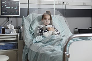 Ill kid resting in children healthcare facility patient bed alone while having teddy bear