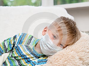 Ill little boy in medicine health-care mask lying on bed