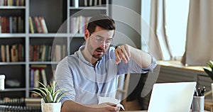 Ill male worker sitting at workplace blowing nose in tissue