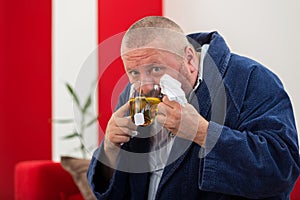 Ill man blowing his nose with paper napkin and drinking tea at home