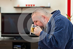 Ill man blowing his nose with paper napkin and drinking tea at home