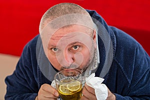 Ill man blowing his nose with paper napkin and drinking tea at home